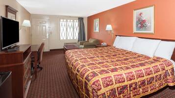 A hotel room with a large bed, a desk with a television, a chair, and a window with curtains.