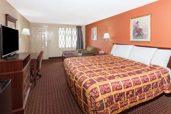 A hotel room with a large bed, a desk with a television, a chair, and a window with curtains.