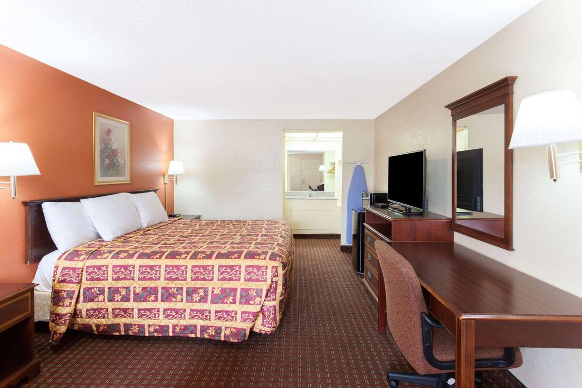 A hotel room with a bed, desk, chair, television, and a mirror.