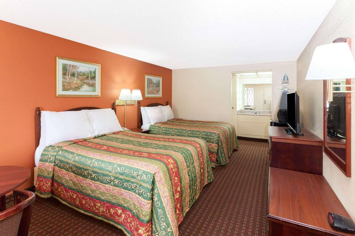 A hotel room with two beds, a desk, a TV, and a bathroom visible through an open door.