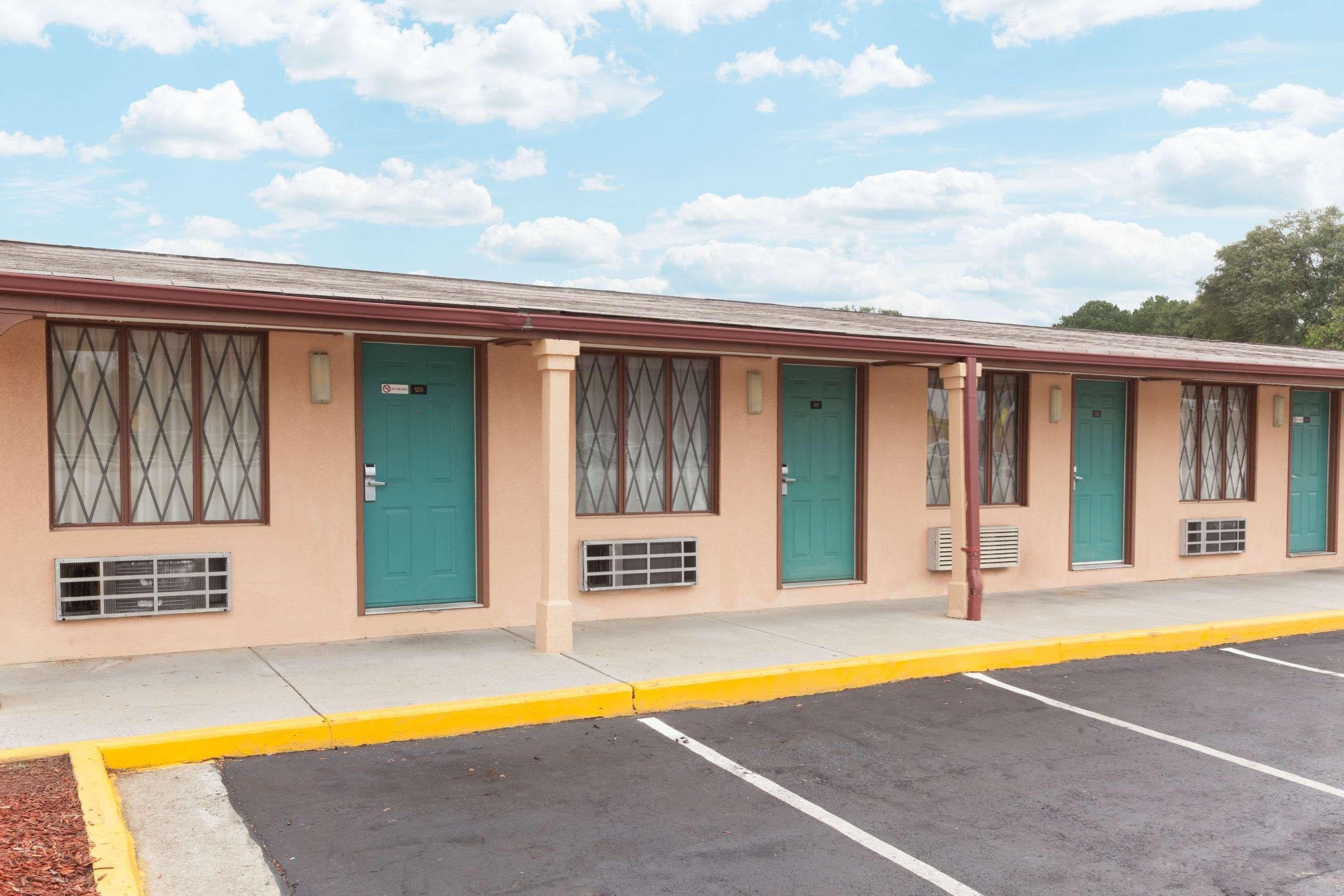 Ein Motel mit einer Reihe von Zimmern, jedes mit einer grünen Tür und einem Fenster mit Rautenmuster.