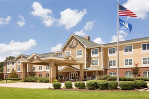 A multi-story hotel with a beige facade, a central entrance with a covered area, and a flagpole with the American flag. - Country Inn & Suites by Radisson, Pineville, LA (Pineville)