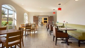 Un vaste espace dédié à la salle à manger, avec des tables et des chaises en bois, un canapé vert et des lampes suspendues rouges.