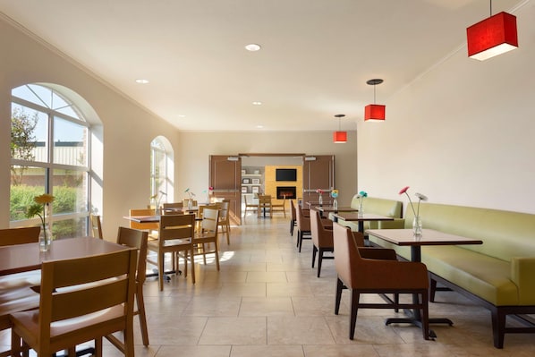 A spacious dining area with wooden tables and chairs, a green sofa, and red pendant lights. - Country Inn & Suites by Radisson, Pineville, LA (Pineville)