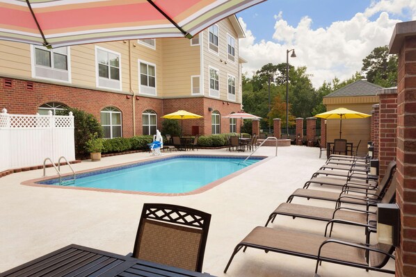 A swimming pool with lounge chairs and umbrellas, surrounded by a brick building with windows and a white fence. - Country Inn & Suites by Radisson, Pineville, LA (Pineville)