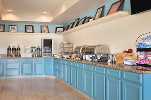 A kitchen area with blue cabinetry, a countertop with various food items and appliances, and a tiled backsplash. - Country Inn & Suites by Radisson, Pineville, LA (Pineville)