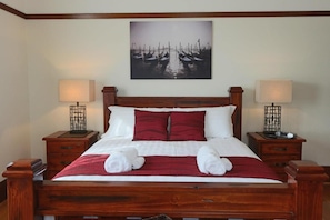 A neatly made bed with a red and white bedspread, two bedside tables with lamps, and a wall-mounted picture of boats. - Moonah Amy Cottage Apartments (Hobart)