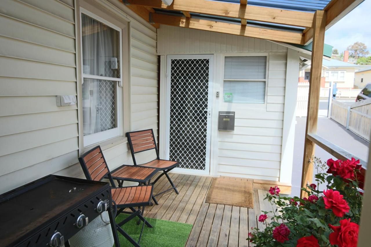 Un patio cubierto con una parrilla, dos sillas, una puerta con mosquitero y una terraza de madera.