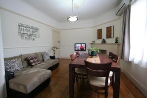 A living room with a sofa, dining table, chairs, a TV, and a fireplace. - Moonah Amy Cottage Apartments (Hobart)