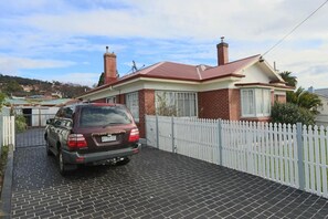 A house with a brick exterior, a red roof, and a white picket fence. - Moonah Amy Cottage Apartments (Hobart)