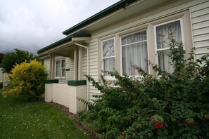 A single-story house with a front porch, a small garden with bushes and a tree, and a clear sky. - Moonah Amy Cottage Apartments (Hobart)