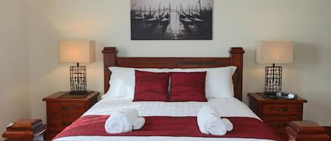 A neatly made bed with a red and white bedspread, two bedside tables with lamps, and a wall-mounted picture of boats.