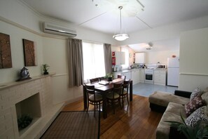 A modern kitchen with white cabinets, a dining table with chairs, a fireplace, and a living area with a sofa. - Moonah Amy Cottage Apartments (Hobart)