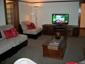 A living room with a sofa, armchair, coffee table, TV, and wooden cabinet. - Moonah Amy Cottage Apartments (Hobart)