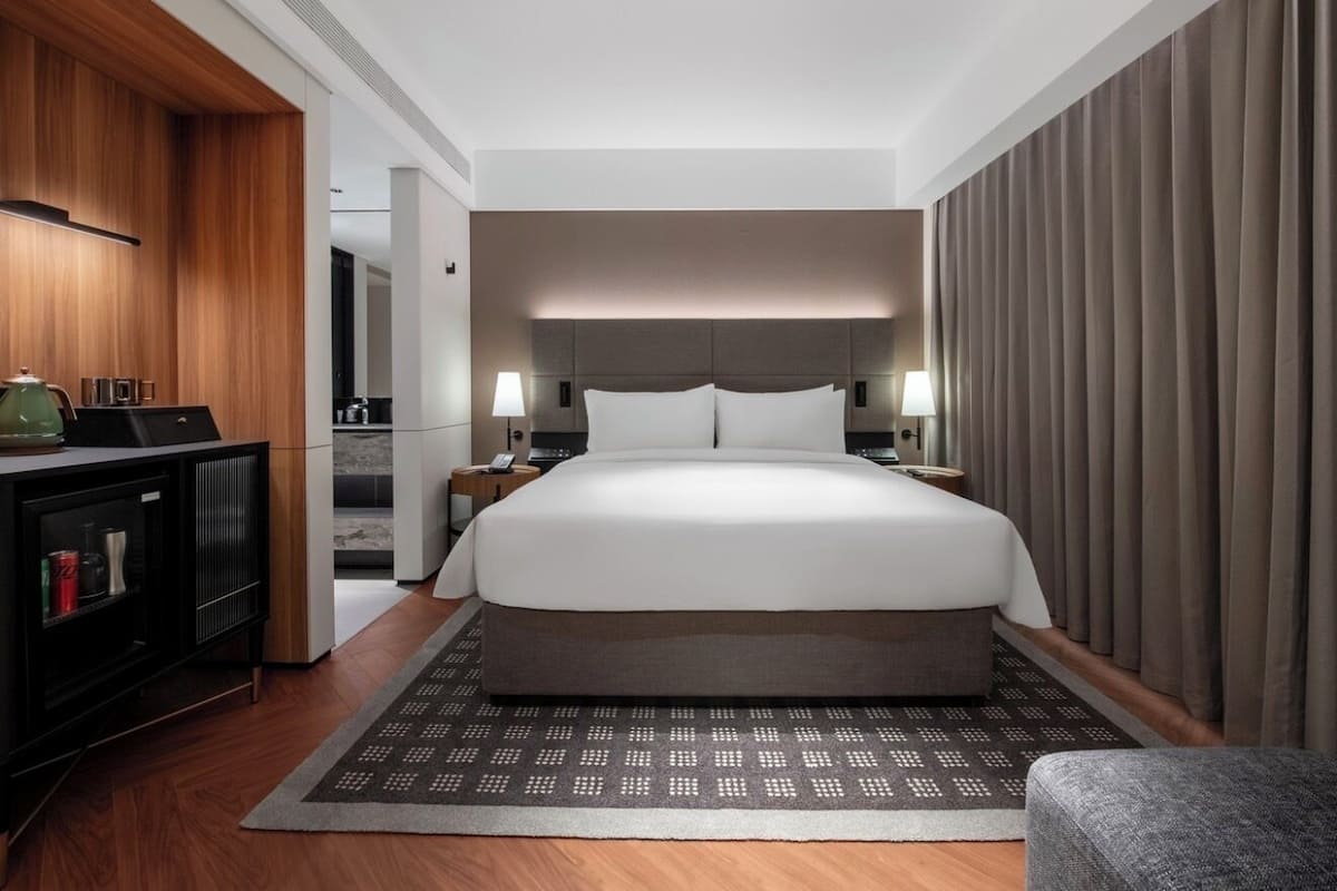 A hotel room with a large bed, bedside tables, a desk with a lamp, and a wardrobe.