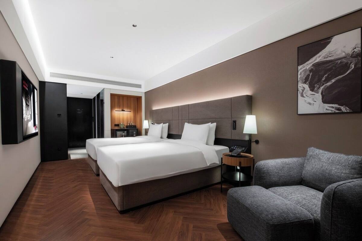 A hotel room with a large bed, a sofa, a nightstand, and a wall-mounted lamp.