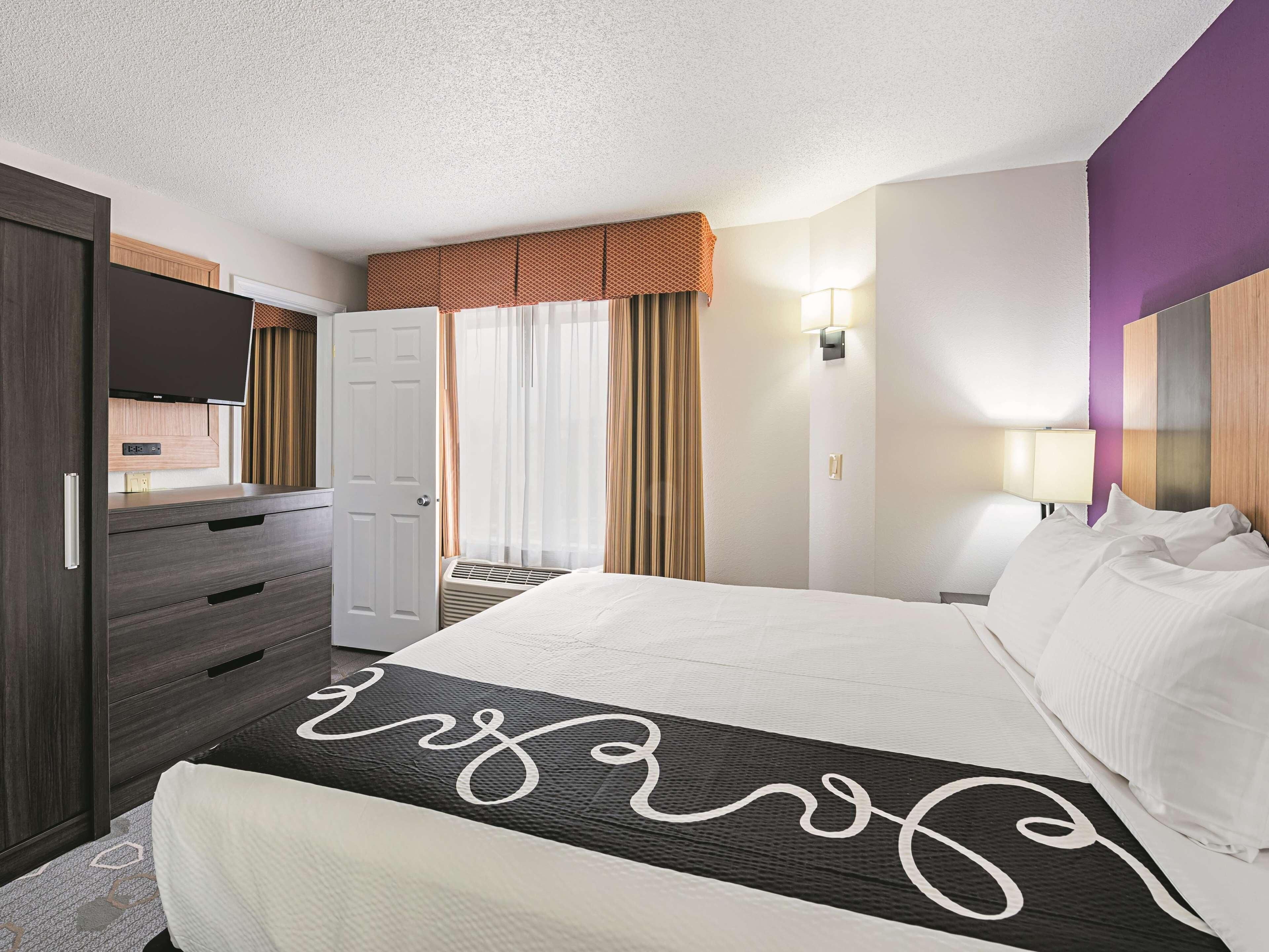 A hotel room with a bed, a dresser, a TV, and a window with curtains.