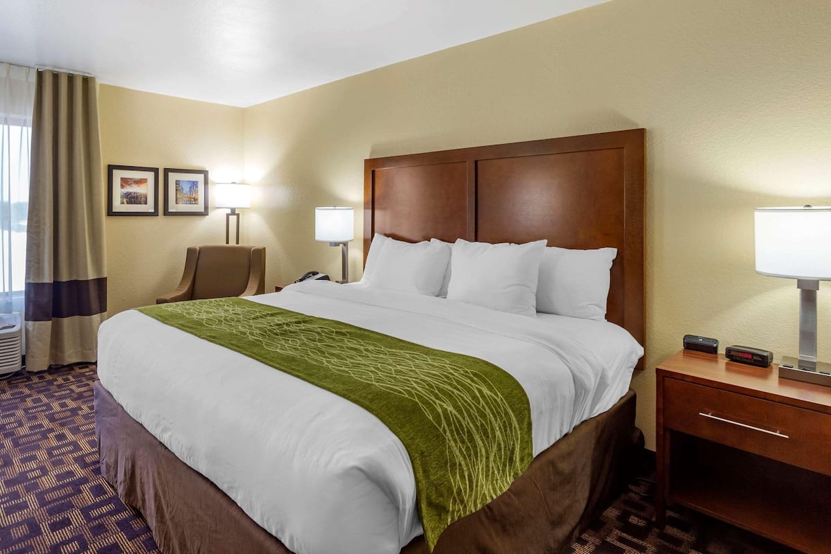 A hotel room with a large bed, two bedside lamps, a chair, a desk, and a nightstand.