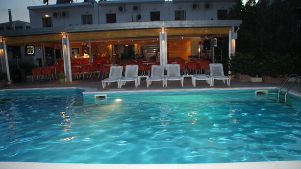 En pool med solstolar och en möblerad uteplats under tak.