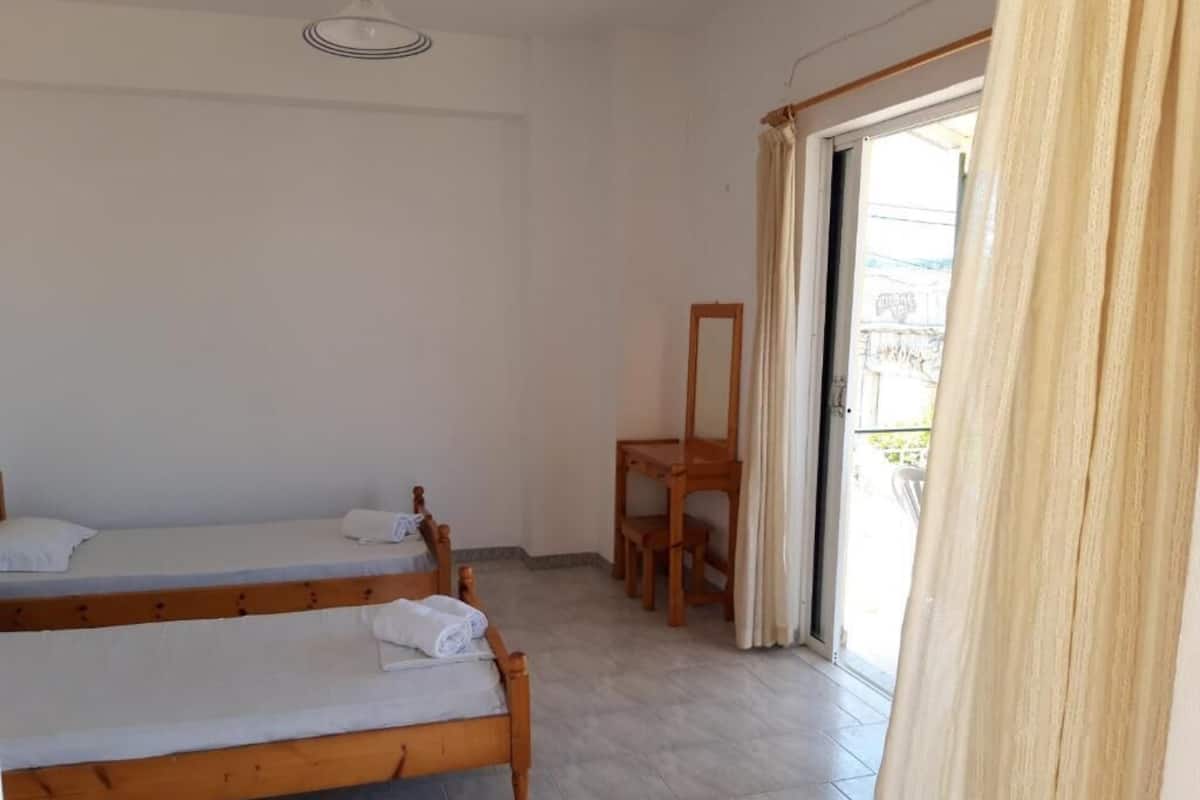 A room with two wooden beds, a wooden chair, a table, and a sliding glass door to the outside.