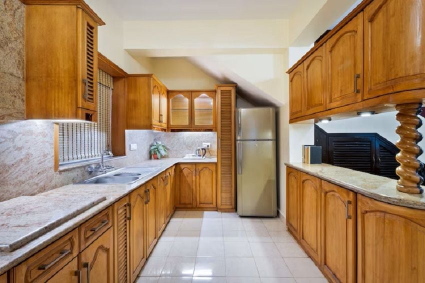 Una cocina con armarios de madera, encimera de mármol, refrigerador de acero inoxidable y suelo de baldosas.
