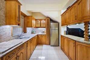 A kitchen with wooden cabinets, a marble countertop, a stainless steel refrigerator, and a tiled floor. - De Mandarin Beach Resort Suites & Villas Goa (Candolim)