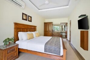 A bedroom with a bed, bedside table, and a TV mounted on the wall. - De Mandarin Beach Resort Suites & Villas Goa (Candolim)