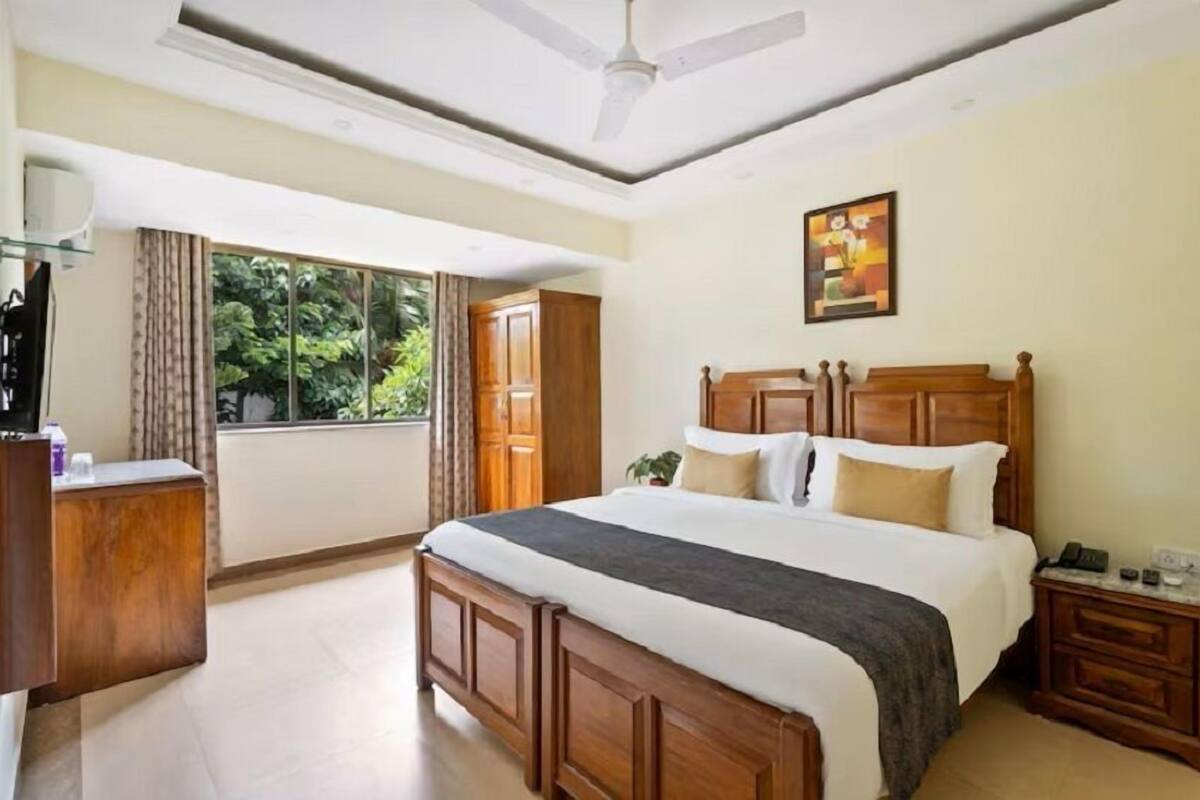 A bedroom with a large bed, wooden headboard, a nightstand, a desk, a ceiling fan, and a window with curtains.