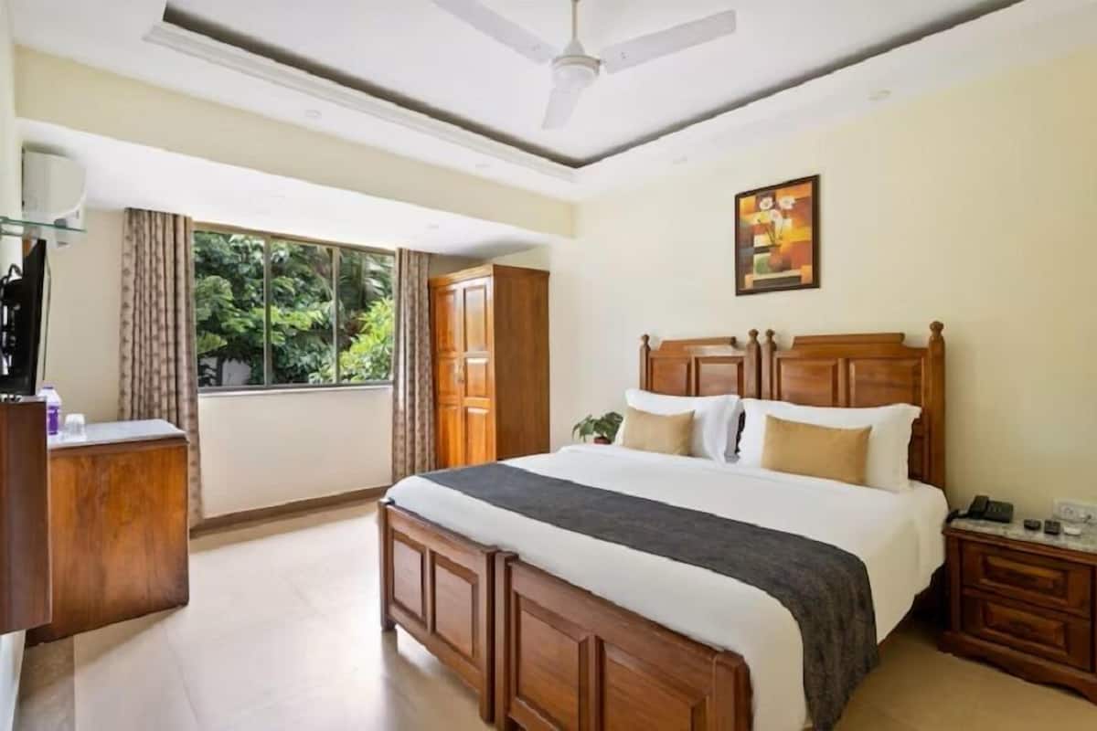 A bedroom with a large bed, wooden headboard, a nightstand, a desk, a ceiling fan, and a window with curtains.