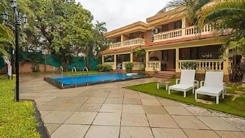 A two-story building with a swimming pool, outdoor seating, and a well-maintained garden.