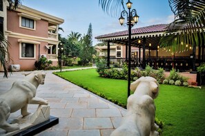 A courtyard with a statue, a covered seating area, and a building with a balcony. - De Mandarin Beach Resort Suites & Villas Goa (Candolim)