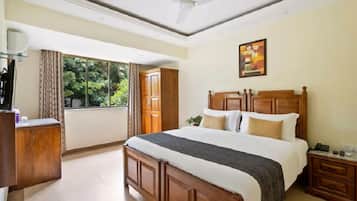 A bedroom with a large bed, wooden headboard, a nightstand, a desk, a ceiling fan, and a window with curtains.