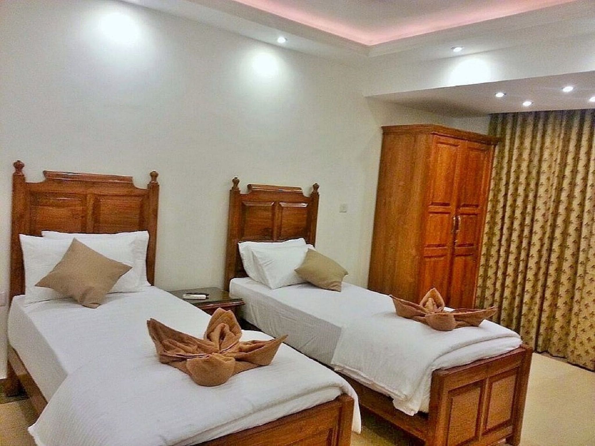 Una habitación de hotel con dos camas de madera, ropa de cama blanca y un armario de madera.