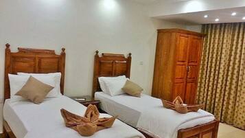 Una habitación de hotel con dos camas de madera, ropa de cama blanca y un armario de madera.