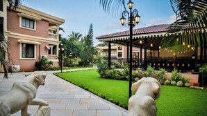 A courtyard with a statue, a covered seating area, and a building with a balcony. - De Mandarin Beach Resort Suites & Villas Goa (Candolim)