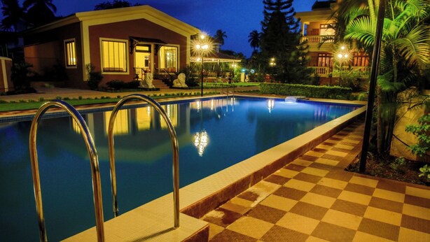 A swimming pool with metal ladders, a checkered walkway, and a building with a balcony in the background. - De Mandarin Beach Resort Suites & Villas Goa (Candolim)