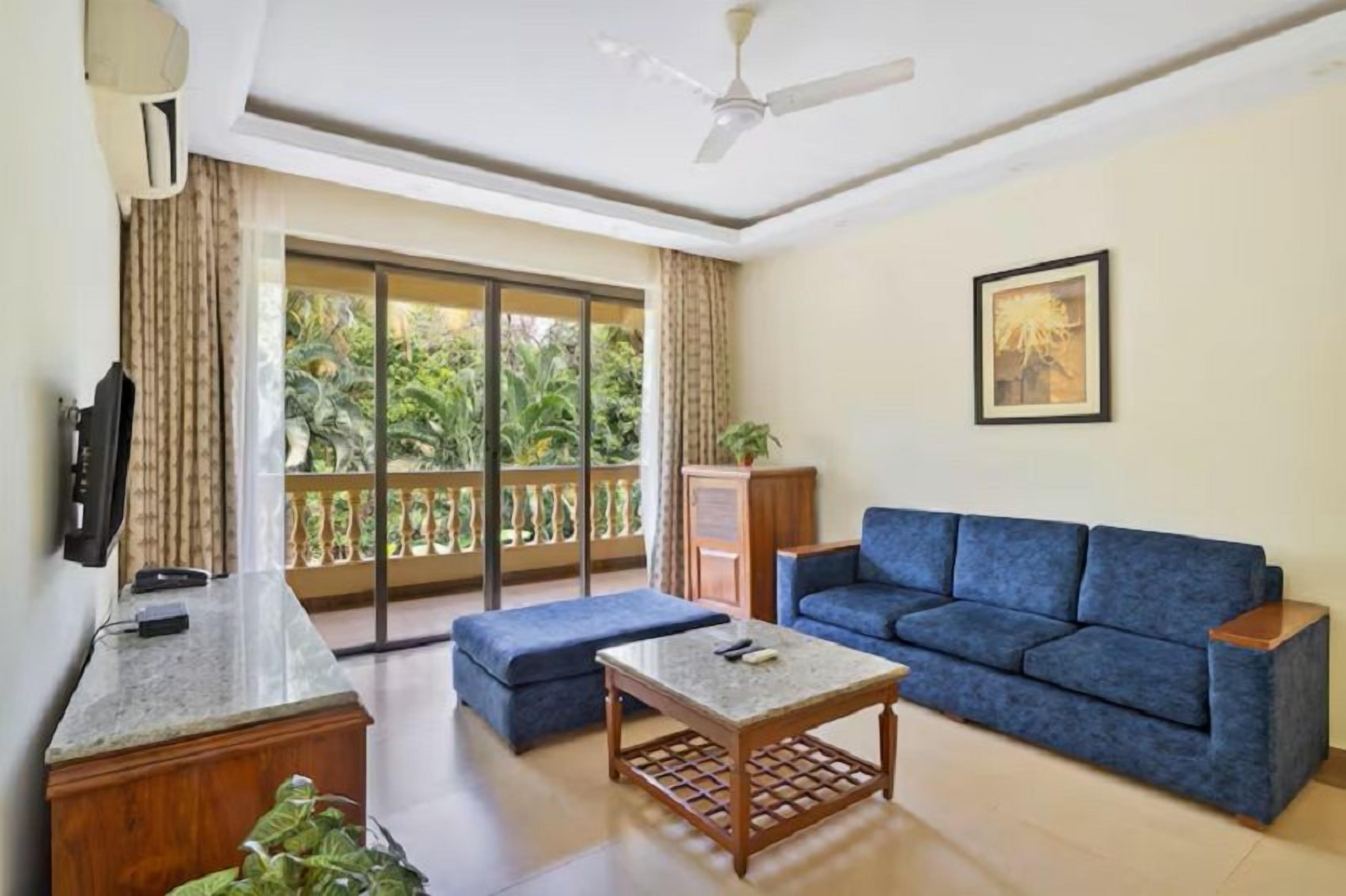 Sala de estar com um sofá azul, uma mesinha, uma TV e uma varanda com vista para o verde.