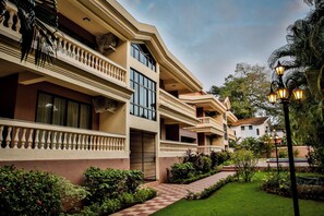 A multi-story hotel with balconies, a checkered pathway, and lush greenery. - De Mandarin Beach Resort Suites & Villas Goa (Candolim)