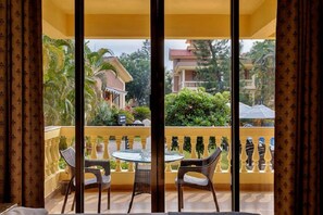 A balcony with a table and chairs, a yellow railing, and a view of buildings and greenery. - De Mandarin Beach Resort Suites & Villas Goa (Candolim)