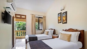 A hotel room with two beds, a TV, a window with curtains, and a balcony with a view of greenery. - De Mandarin Beach Resort Suites & Villas Goa (Candolim)