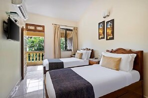 A hotel room with two beds, a TV, a window with curtains, and a balcony with a view of greenery. - De Mandarin Beach Resort Suites & Villas Goa (Candolim)