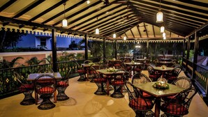 An outdoor dining area with tables and chairs, a covered roof, and a view of the surrounding landscape. - De Mandarin Beach Resort Suites & Villas Goa (Candolim)