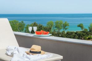 Een balkon met uitzicht op de oceaan, een bord met watermeloen en een hoed op een stoel.