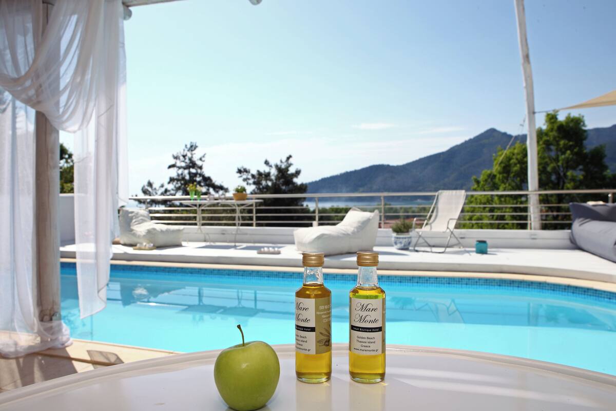 A poolside table with two bottles of Mare Monte and a green apple, overlooking a pool with a mountain view.