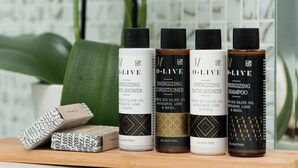 Una estantería con cuatro botellas de aceite de oliva, una pastilla de jabón y una planta en maceta.