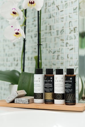 A shelf with four bottles of olive oil products, a bar of soap, and a potted plant. - Mare Monte Boutique Hotel (Thasos)