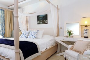 Een hemelbed met een baldakijn, een nachtkastje met een lamp en een schilderij aan de muur.