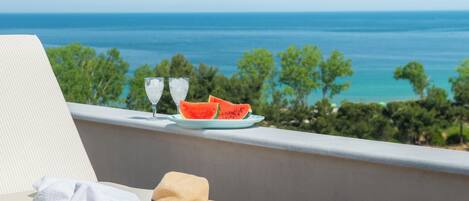 A balcony with a view of the ocean, a plate with watermelon slices, and a hat on a chair.