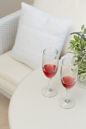 Duas taças de vinho sobre uma mesa branca, com uma almofada branca e uma planta ao fundo.