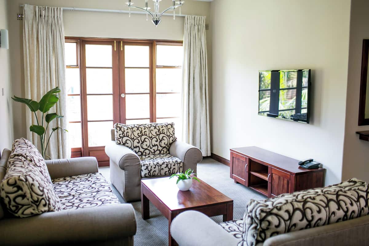 A living room with a sofa set, a coffee table with a plant, a TV mounted on the wall, and a wooden cabinet.
